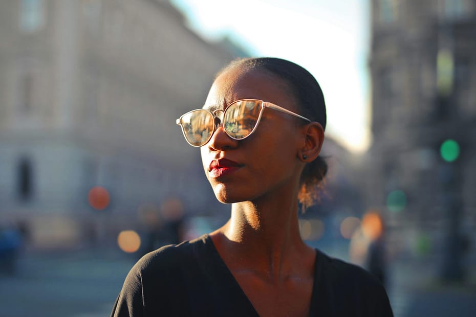 A fashionable woman wearing sunglasses in a vibrant city street during the day.